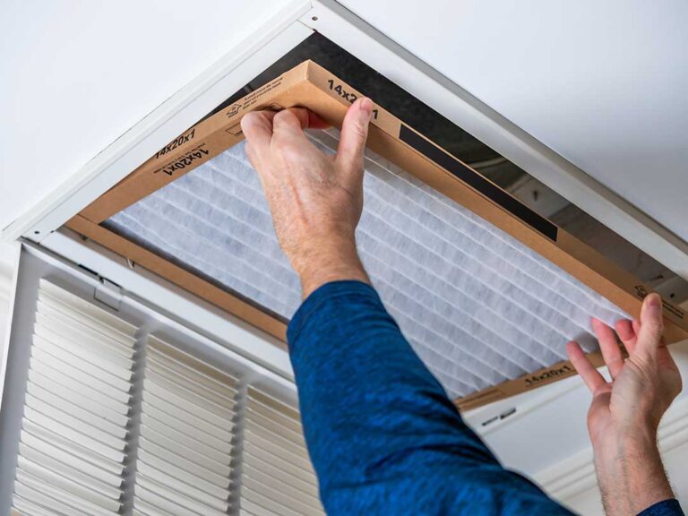 A technician checks the outdoor unit of a residential air conditioner on a sunny day.
